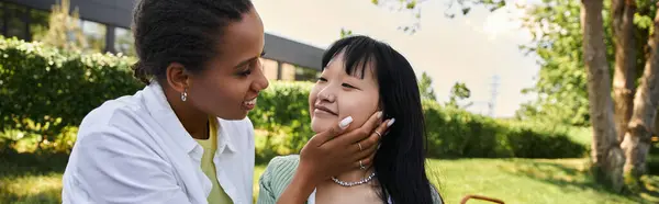 Two young women, one African American and the other Asian, share a tender moment during a picnic in a park. — Stock Photo