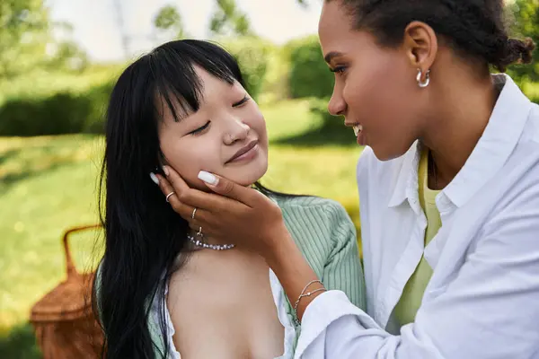 Una giovane donna tocca delicatamente il viso della sua ragazza mentre condividono un momento tenero durante un picnic. — Foto stock