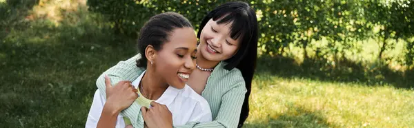 A young lesbian couple, one African American and one Asian, share a loving embrace during a picnic in a park. — Stock Photo
