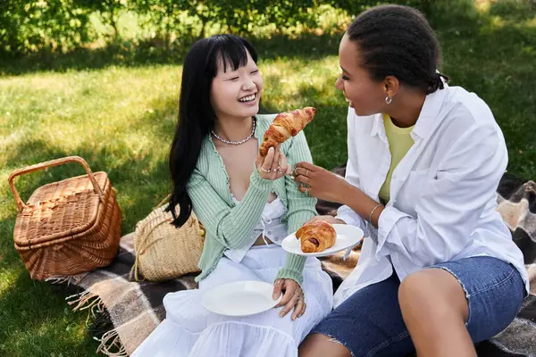 Ein junges lesbisches Paar teilt ein Lachen und ein Croissant während eines Picknicks im Park. — Stock Photo