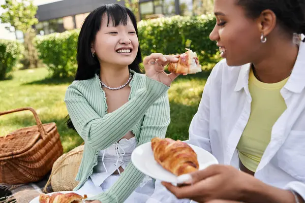 Due giovani donne che si godono un picnic insieme, condividendo risate e croissant in una giornata di sole. — Foto stock