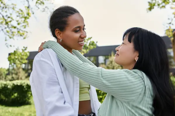 A lesbian couple, one African American and one Asian, share a loving embrace while enjoying a sunny day outdoors. — Stock Photo