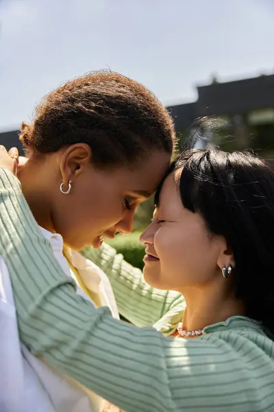 Two young women, one African American and one Asian, embrace, their foreheads touching in a loving gesture. — Stock Photo