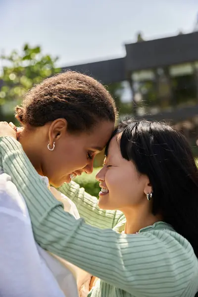 A young African American woman embraces her Asian partner with a smile, sharing a tender moment in the sunshine. — Stock Photo