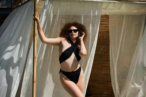 A woman in a black swimsuit, sunlight streaming through sheer curtains behind her. — Stock Photo