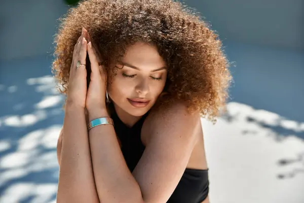 A woman with curly hair, wearing a black swimsuit, rests her head on her arms, eyes closed, enjoying the summer sun — Stock Photo