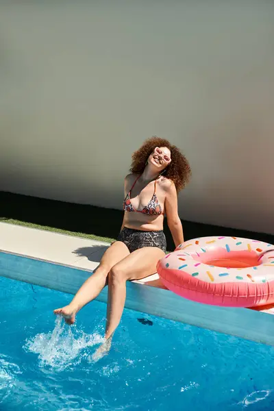 A woman in a bikini enjoys a sunny day at the pool, dipping her toes in the water and laughing. — Stock Photo