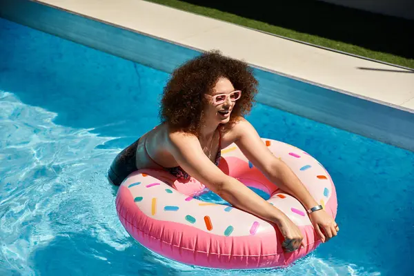 A woman with curly hair enjoys a sunny day by the pool, floating on a donut-shaped inflatable. — Stock Photo