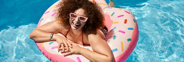 A woman with curly hair smiles while floating on a donut pool float. — Stock Photo
