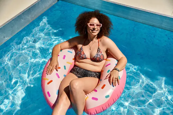 A woman with curly hair relaxes in a pool on a donut-shaped float, enjoying the summer sun. — Stock Photo