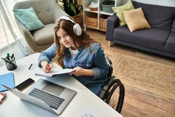 Uma jovem mulher em uma cadeira de rodas trabalha em seu laptop em uma mesa em seu apartamento moderno. — Fotografia de Stock