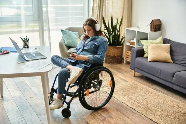 A young woman in a wheelchair sits in a modern apartment, listening to music and using her smartphone. — Stock Photo