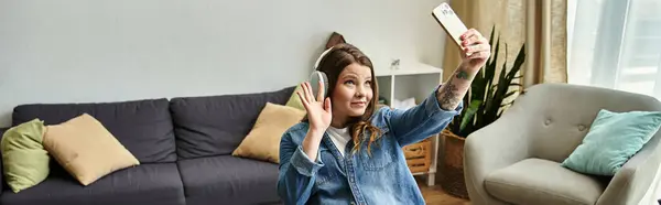 A young woman takes a selfie while wearing headphones in her modern apartment. — Stock Photo