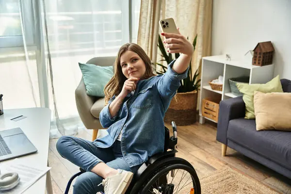 Une jeune femme sourit en prenant un selfie dans son appartement assis dans un fauteuil roulant. — Photo de stock