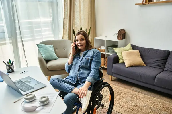 A young woman sits in a wheelchair in her living room, smiling and talking on the phone. — Stock Photo