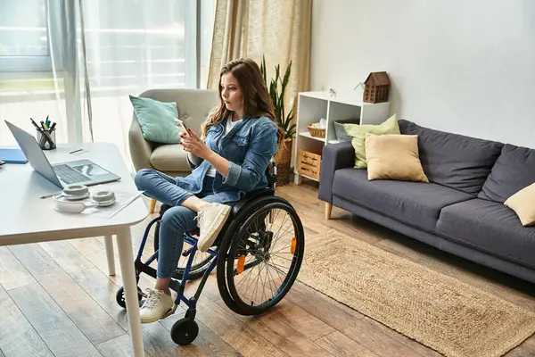 A young woman in a wheelchair sits in a modern apartment, casually scrolling through her smartphone. — Stock Photo