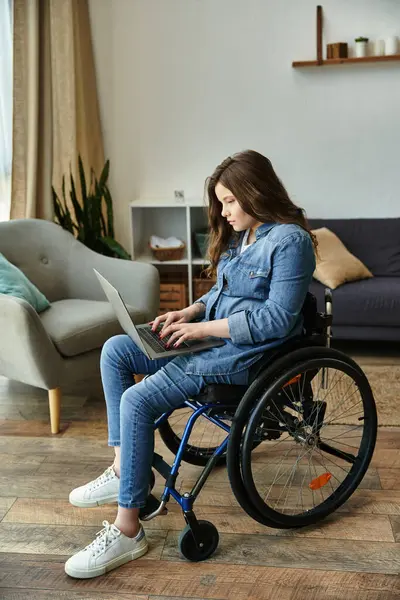 A young woman in a wheelchair works on her laptop in a modern apartment, showcasing a fulfilling life. — Stock Photo