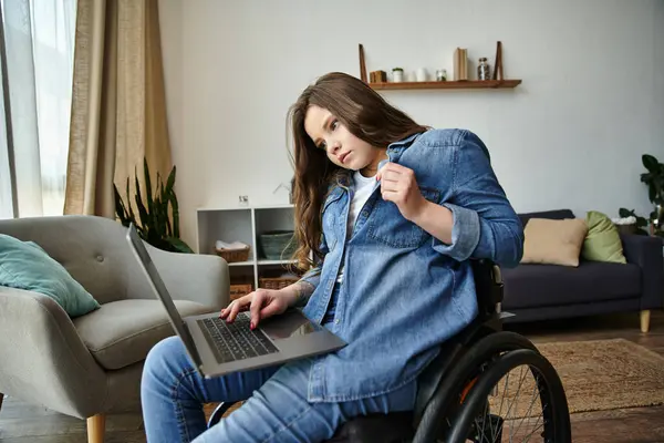 A young woman in a wheelchair uses her laptop while sitting in a modern apartment. — Stock Photo