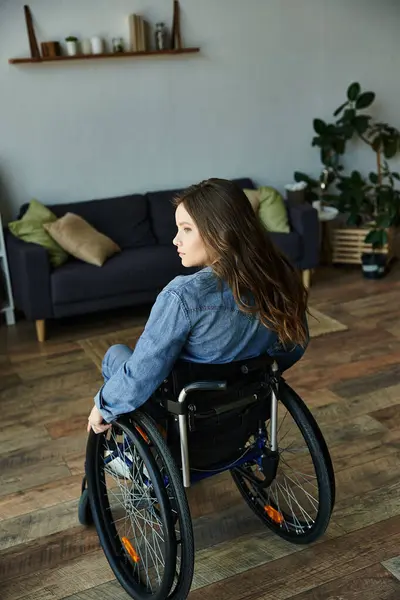 Eine junge Frau sitzt im Rollstuhl in einer modernen Wohnung und blickt aus einem Fenster. — Stockfoto