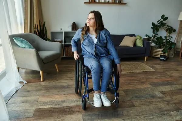 A young woman in a wheelchair sits in a modern apartment, gazing out the window, contemplating the day ahead. — Stock Photo