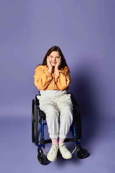 Eine junge Frau in legerer Kleidung lächelt im Rollstuhl und berührt ihr Gesicht mit beiden Händen. Der Hintergrund ist lila und elegant — Stockfoto