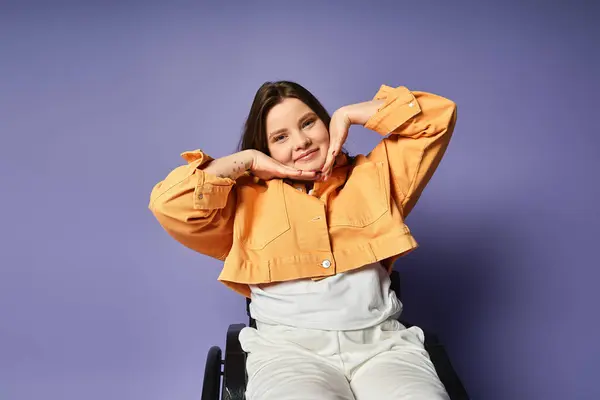 Eine junge Frau im Rollstuhl posiert in einem Atelier mit lila Hintergrund, lässig gekleidet. — Stockfoto