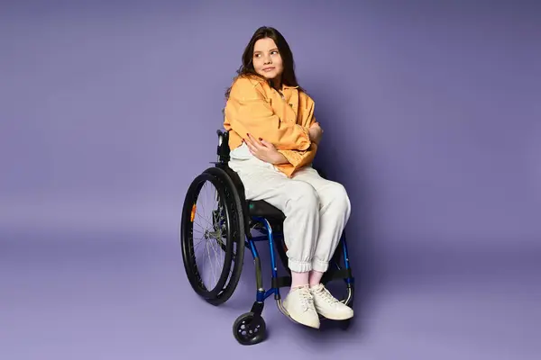 Una joven sentada en una silla de ruedas, vestida con ropa casual, sobre un fondo púrpura. — Stock Photo