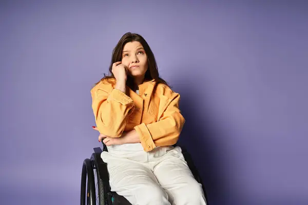 A young woman in a wheelchair, wearing a trendy casual outfit, sits in a studio against a purple backdrop. — Stock Photo