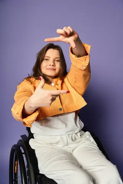 A young woman in a wheelchair, wearing a trendy yellow jacket and white pants, poses in a studio with a purple background. — Stock Photo