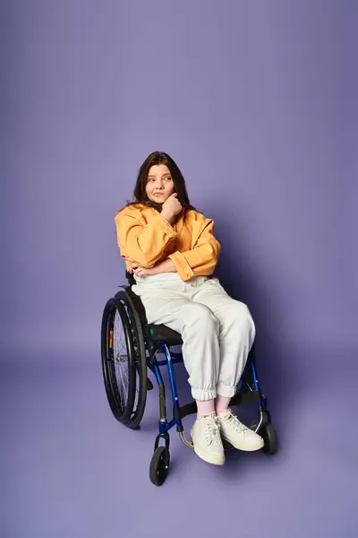 A young woman in a wheelchair sits against a purple background, thoughtfully resting her chin in her hand. — Stock Photo