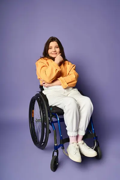 A young woman with long brown hair sits in a wheelchair against a purple backdrop, smiling and looking at the camera. — Stock Photo