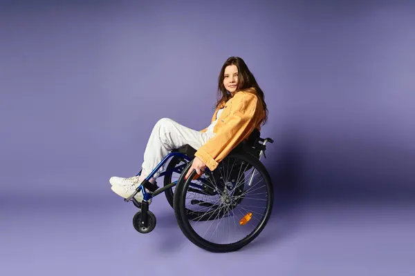 Une jeune femme en tenue décontractée s'assoit dans un fauteuil roulant sur fond violet. — Photo de stock