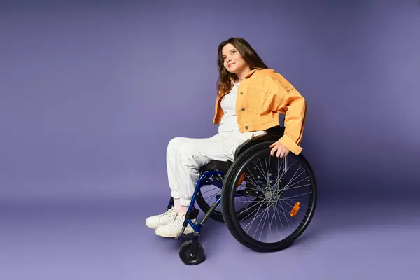 Une jeune femme en fauteuil roulant s'assoit avec désinvolture sur un fond de studio violet. Elle porte un pantalon blanc et une veste jaune. — Photo de stock