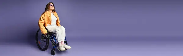 A young woman wearing trendy casual attire sits in a wheelchair against a purple backdrop. — Stock Photo