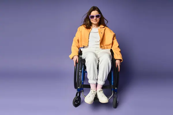 A young woman in a wheelchair poses in a studio with a purple background. She wears sunglasses and a yellow jacket. — Stock Photo