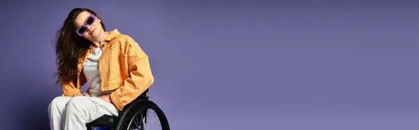 Une jeune femme en fauteuil roulant et tenue décontractée tendance pose sur un fond violet. — Photo de stock