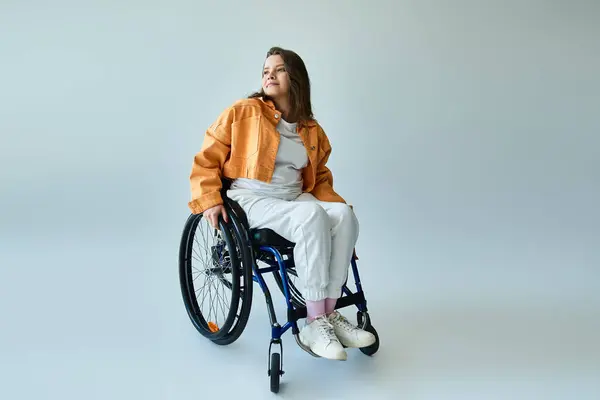 A young woman with long brown hair sits in a wheelchair in a studio setting, looking away from the camera. — Stock Photo