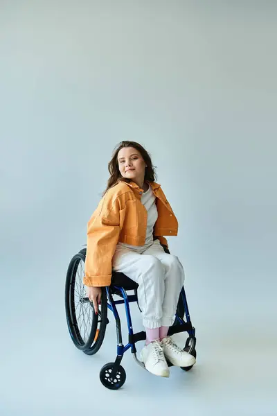 A young woman with long brunette hair sits in a wheelchair in a studio setting. She wears casual clothing and smiles at the camera. — Stock Photo