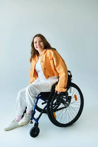 A young brunette woman smiles brightly as she sits in a wheelchair in a studio setting with a grey background. — Stock Photo