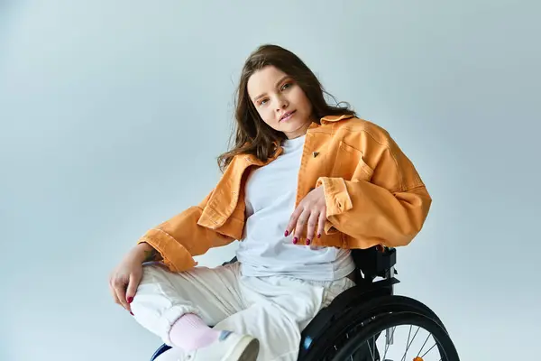 Eine junge Frau im Rollstuhl, in einer stylischen orangefarbenen Jacke und weißer Hose, posiert in einem Studio. — Stockfoto