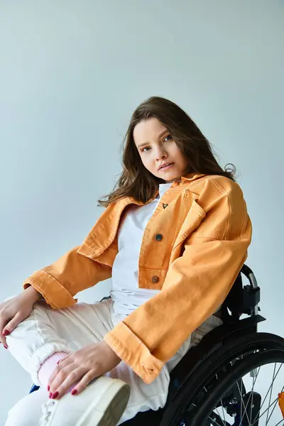 A stylish young brunette woman in a wheelchair poses confidently in a studio setting against a grey background. — Stock Photo