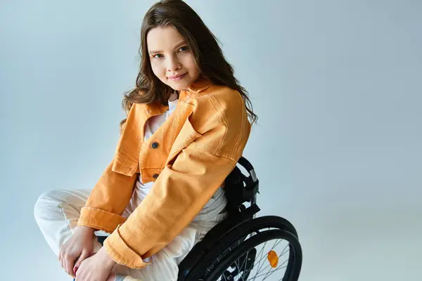 A young woman in a stylish casual outfit sits in a wheelchair against a grey background. — Stock Photo