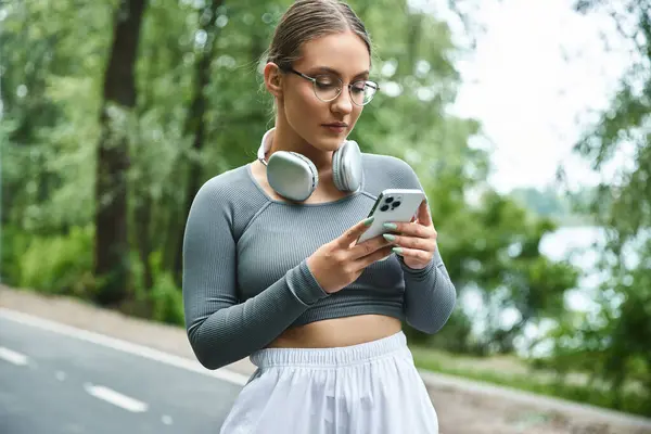 A young woman engages in her smartphone before a workout outdoors, embracing her passion for fitness. — Stock Photo