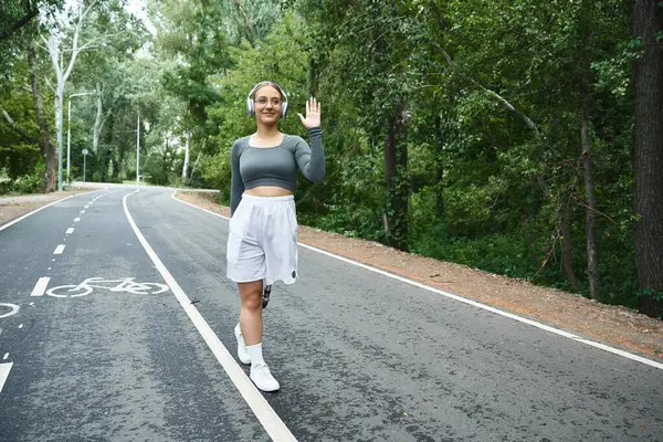 Una giovane donna allena gioiosamente all'aperto, mostrando con sicurezza la sua gamba protesica mentre indossa abbigliamento sportivo. — Foto stock