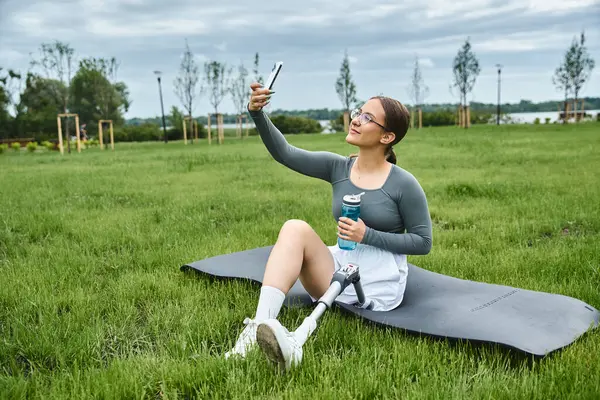 A young woman with a prosthetic leg captures a selfie while working out in a vibrant outdoor setting. — Stock Photo