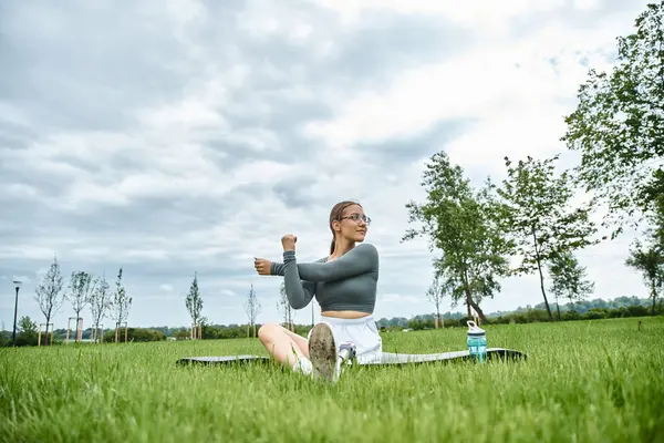A young woman is stretching outdoors on a grassy field, embracing fitness and nature with joy. — Stock Photo