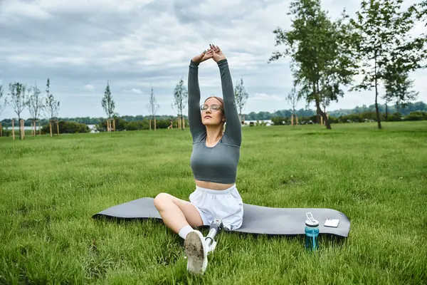 Une jeune femme déterminée en tenue de sport étire son corps sur un tapis, profitant du plein air. — Photo de stock