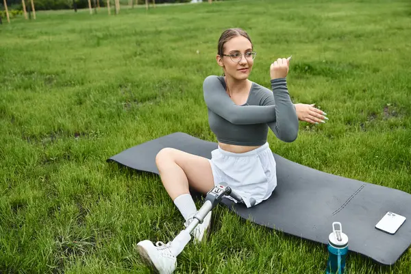 Una donna determinata si allunga all'aria aperta, abbracciando fitness e natura con la sua gamba protesica. — Stock Photo