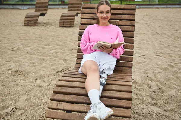 Молода жінка відпочиває на відкритому повітрі, читаючи книгу, насолоджуючись теплим сонцем. — стокове фото