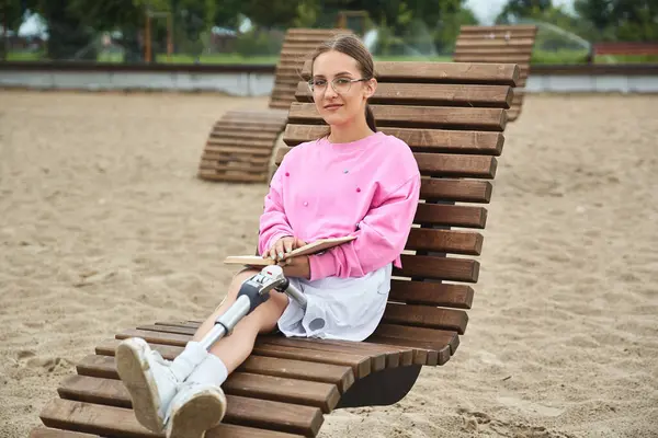 A young woman in sportswear relaxes on a beach chair, enjoying a book by the sandy shore. — Stock Photo